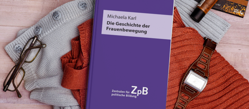 Buch Die Geschichte der Frauenbewegung liegt auf einem Stapel von Gegenständen, die einer weiblichen Person gehören könnten.